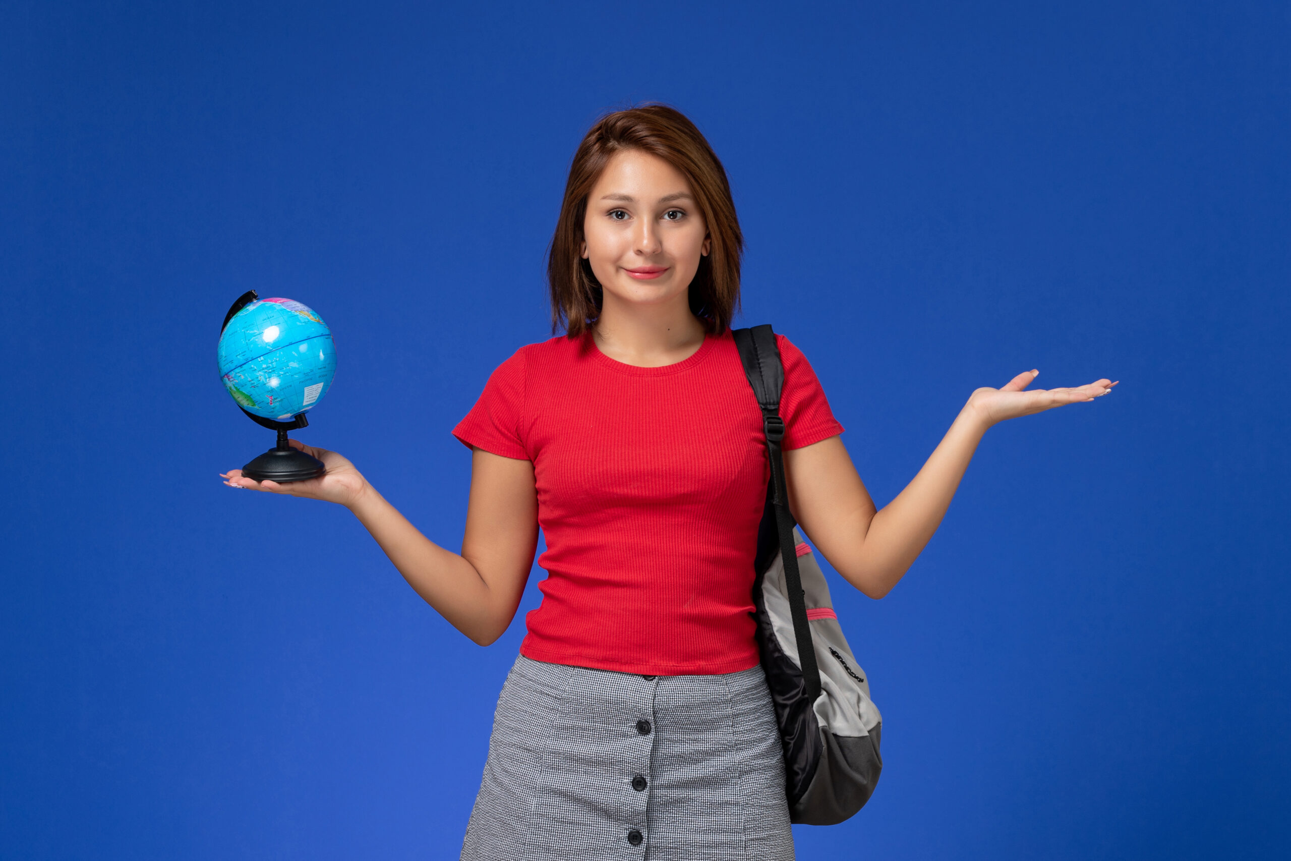 front-view-female-student-red-shirt-with-backpack-holding-little-globe-smiling-blue-wall